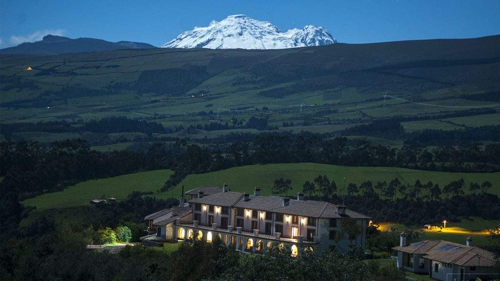La finca iluminada al anochecer con un volcán nevado al fondo