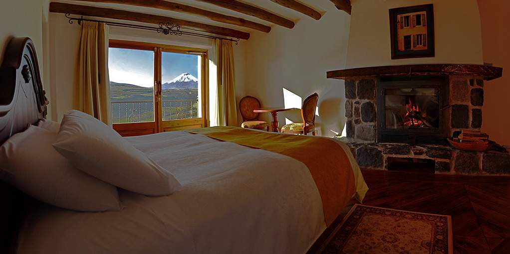 Cama y chimenea en la habitación Antisana con vistas al paisaje andino