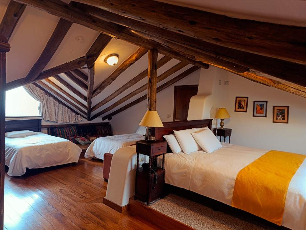 Cama matrimonial y dos camas individuales bajo el techo de madera del ático Ayllu