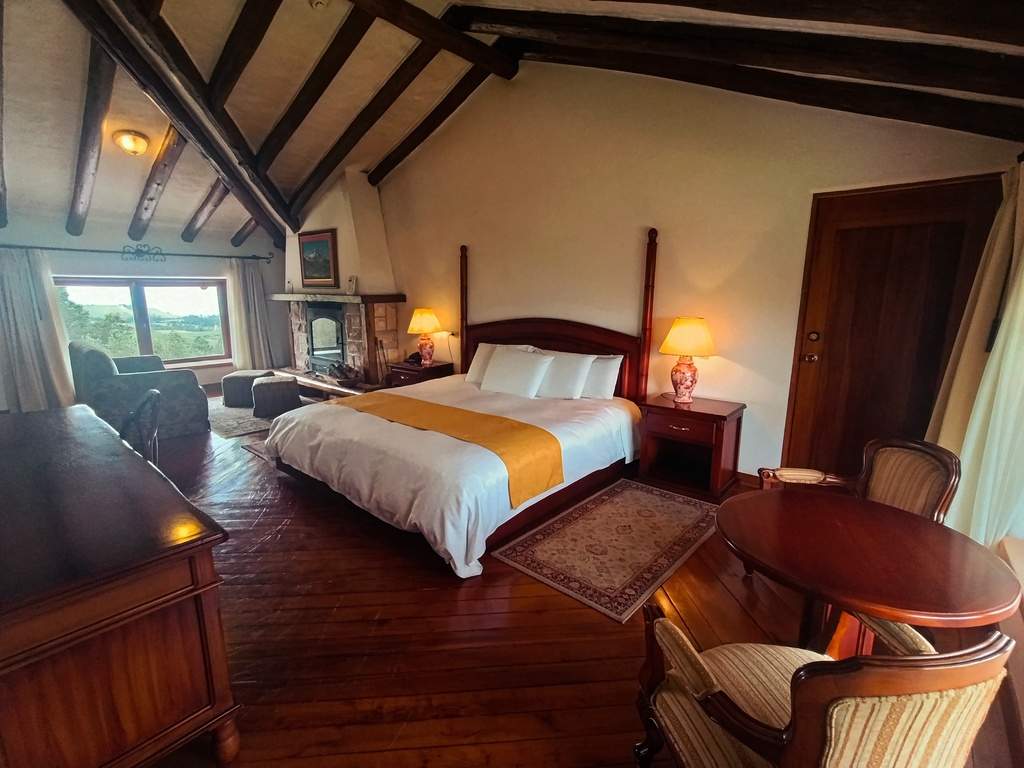 Cama, chimenea y mesa de madera en la habitación Cotopaxi